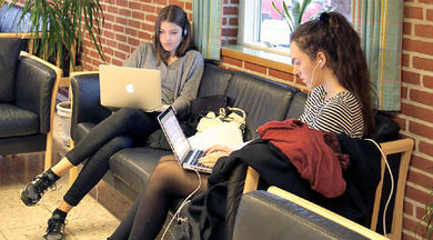 two people sitting on a couch working on laptops