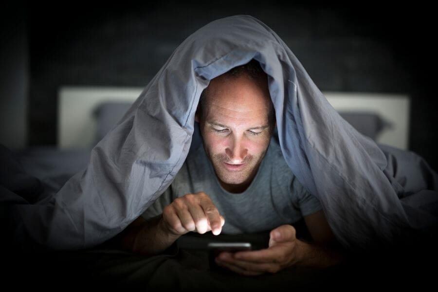 man under covers searching on his phone